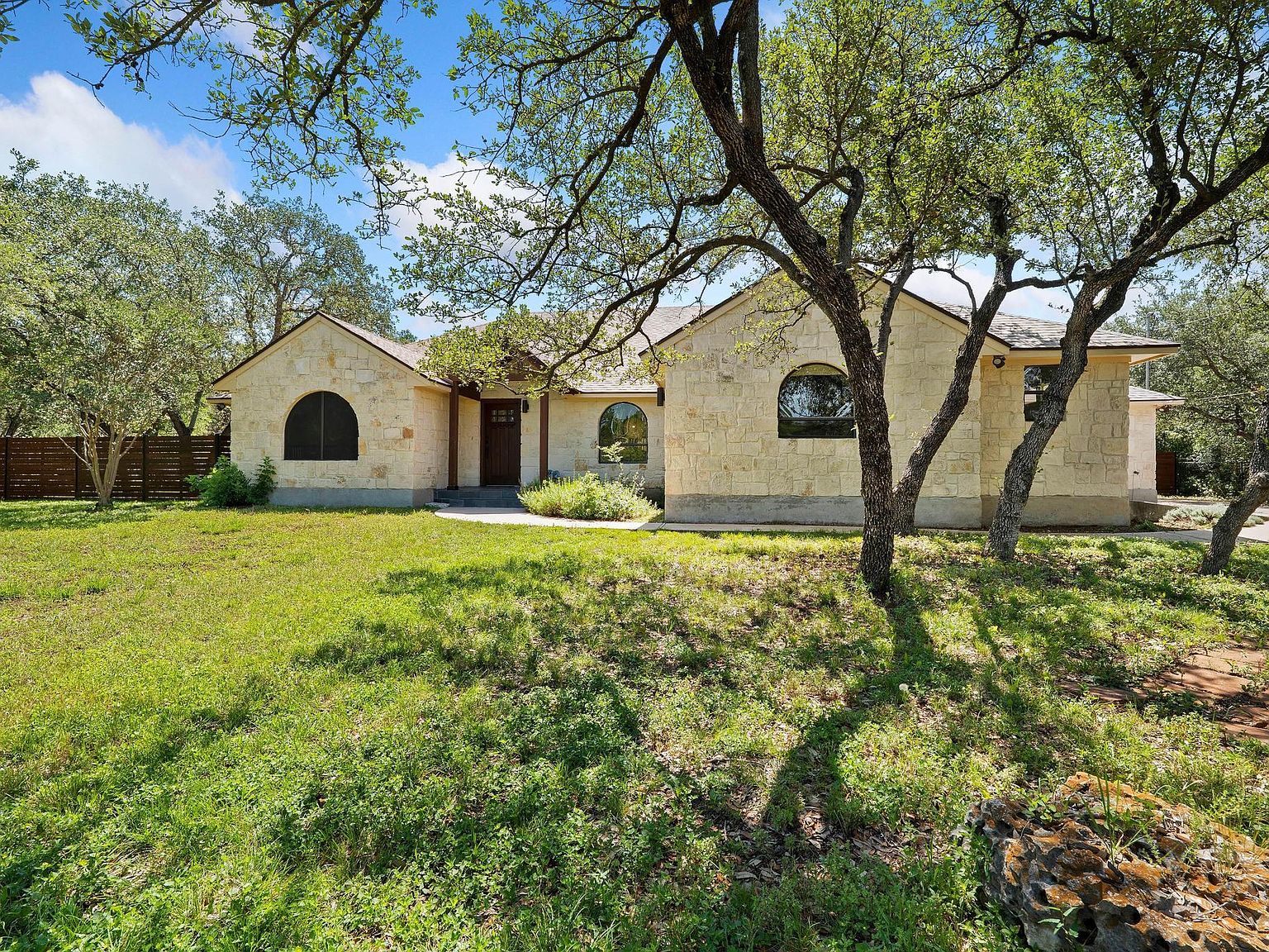 Spanish Ranch front elevation with tile roof and stone accents framed by mature live oaks